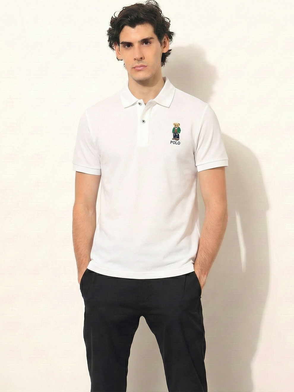 Man wearing a white polo shirt with a logo on a plain background