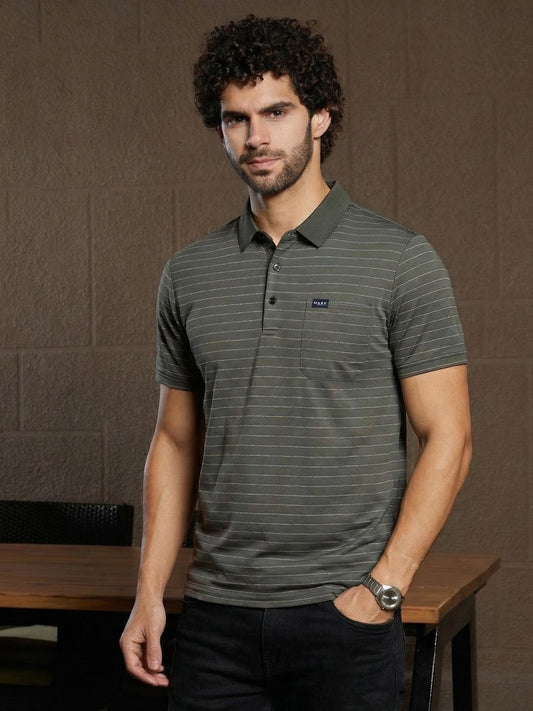 Man wearing a gray striped polo shirt with a brand logo against a brown textured wall.