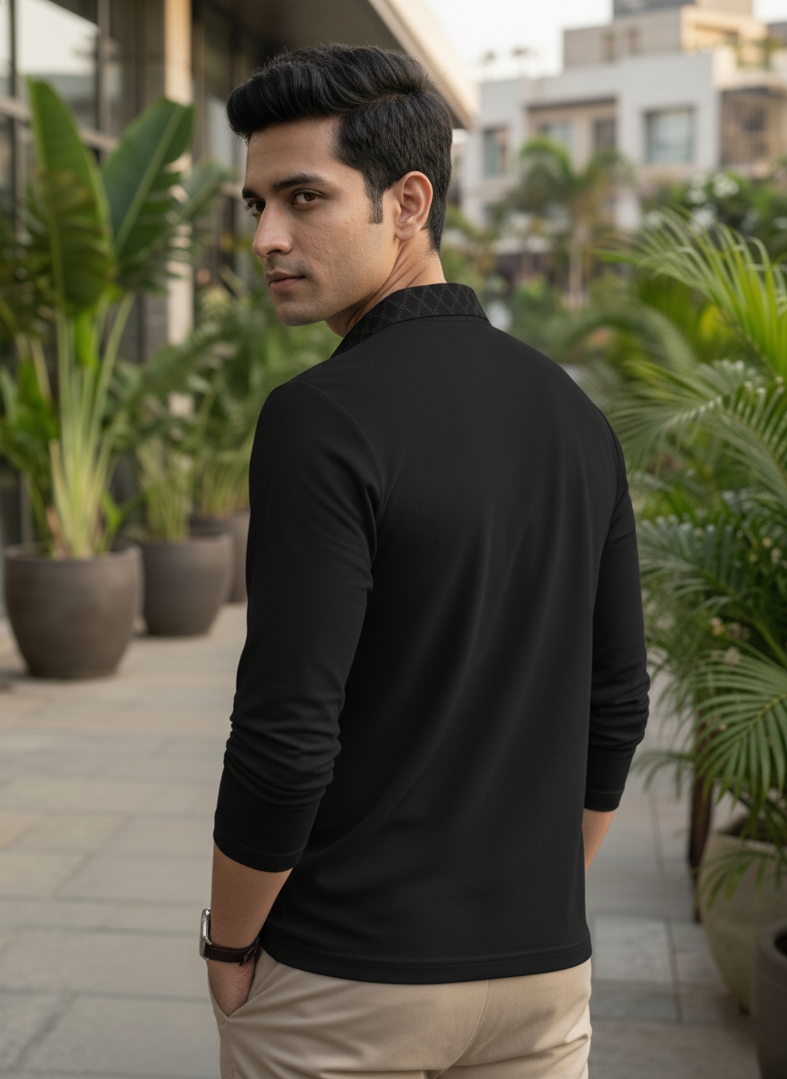 Man wearing a black long-sleeve shirt in an outdoor setting with plants and buildings.