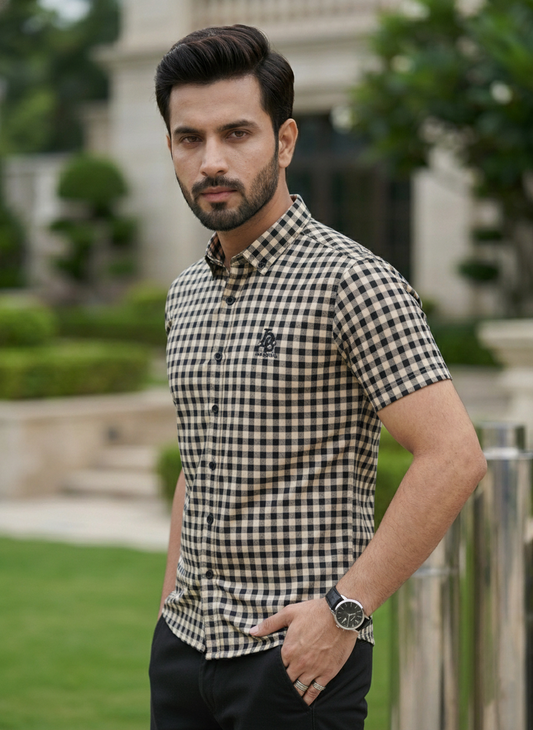 Man wearing a checkered shirt standing outdoors with greenery in the background