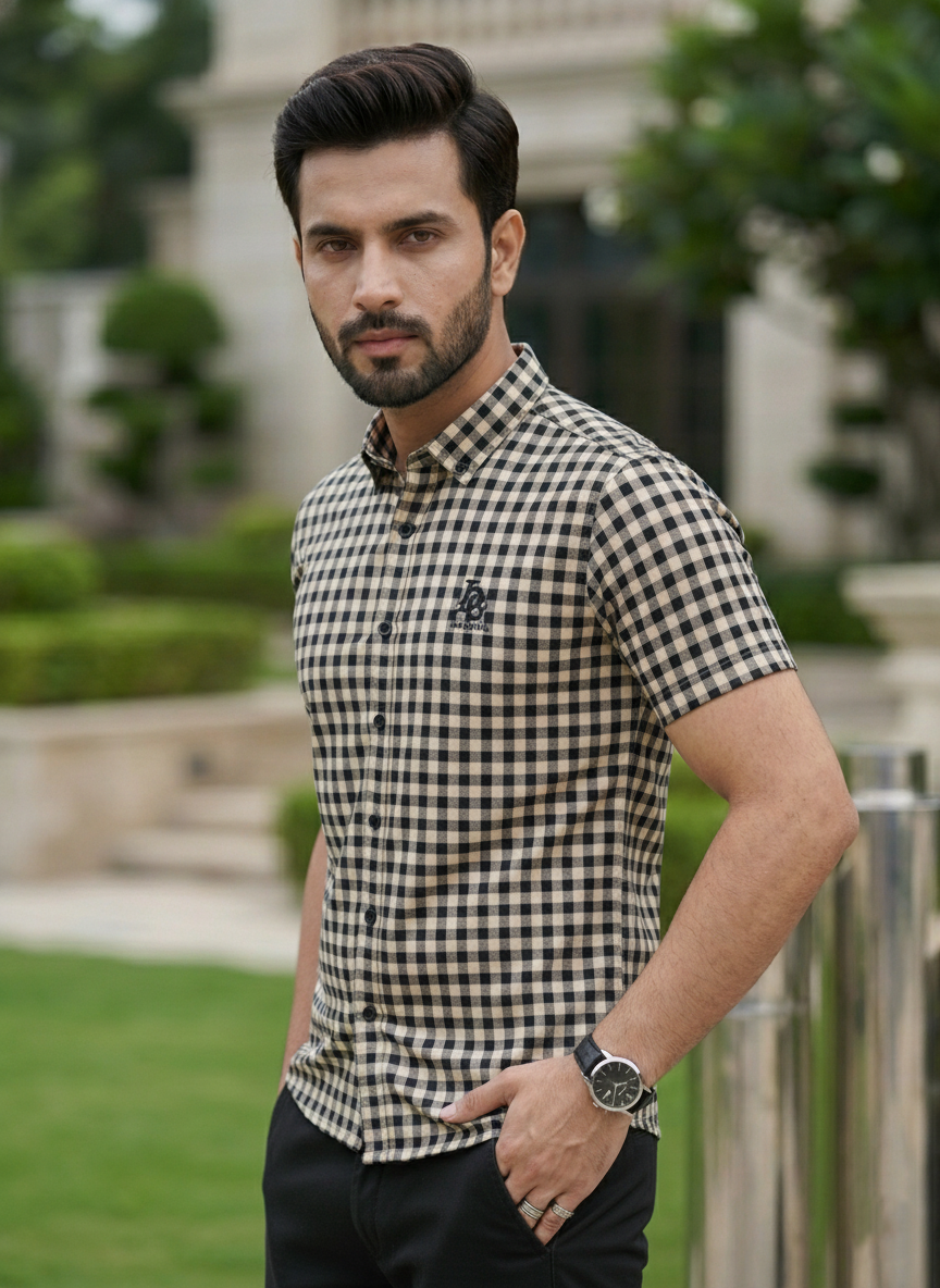 Man wearing a checkered shirt standing outdoors with greenery in the background