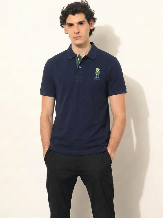 Man wearing a navy blue polo shirt with a logo on a white background