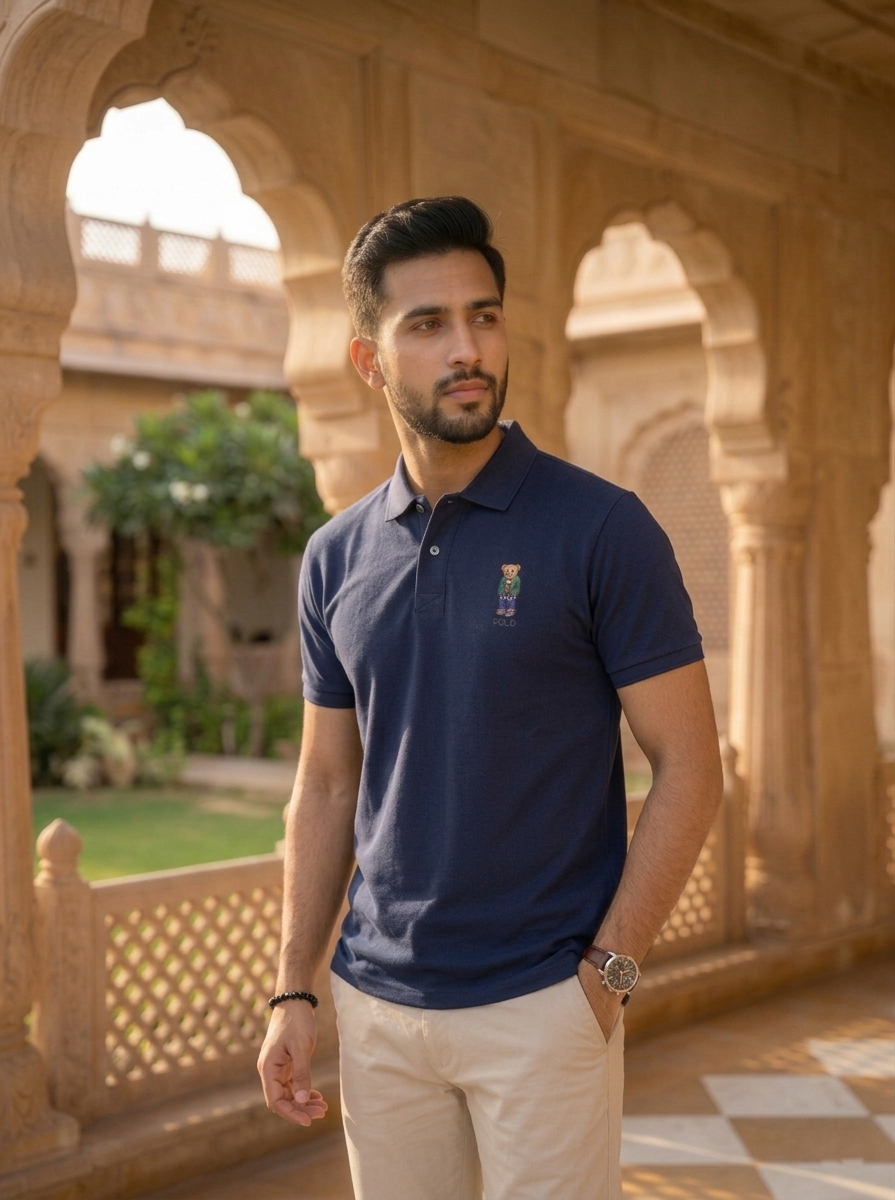 Man wearing a navy blue polo shirt with a logo in an outdoor setting with arches and greenery.