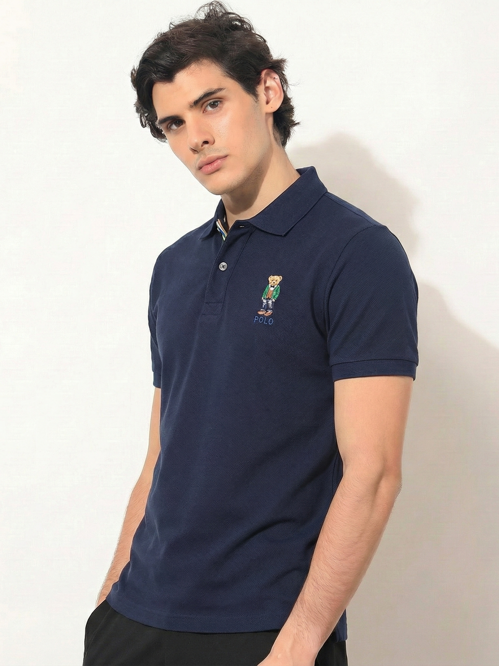 Man wearing a navy blue polo shirt with a logo on a white background