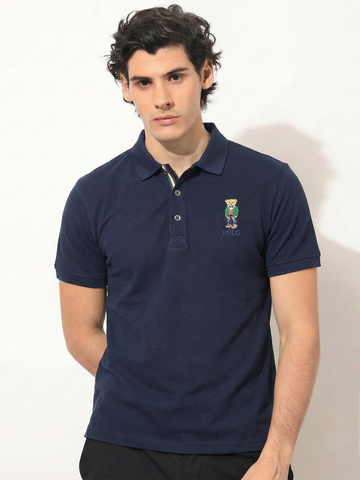 Man wearing a navy blue polo shirt with a small logo on a white background
