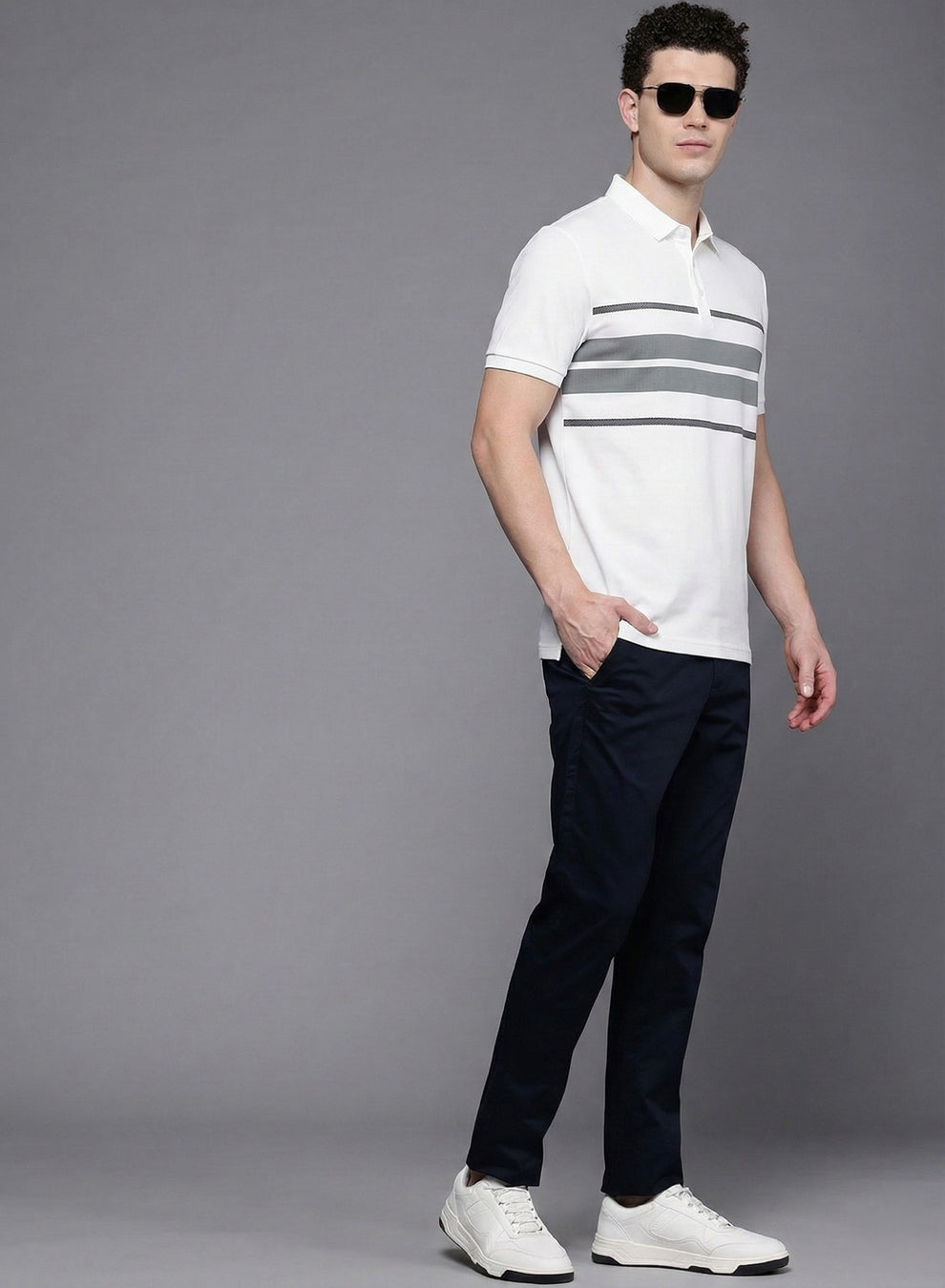 Man wearing a white polo shirt with gray stripes and dark pants on a gray background