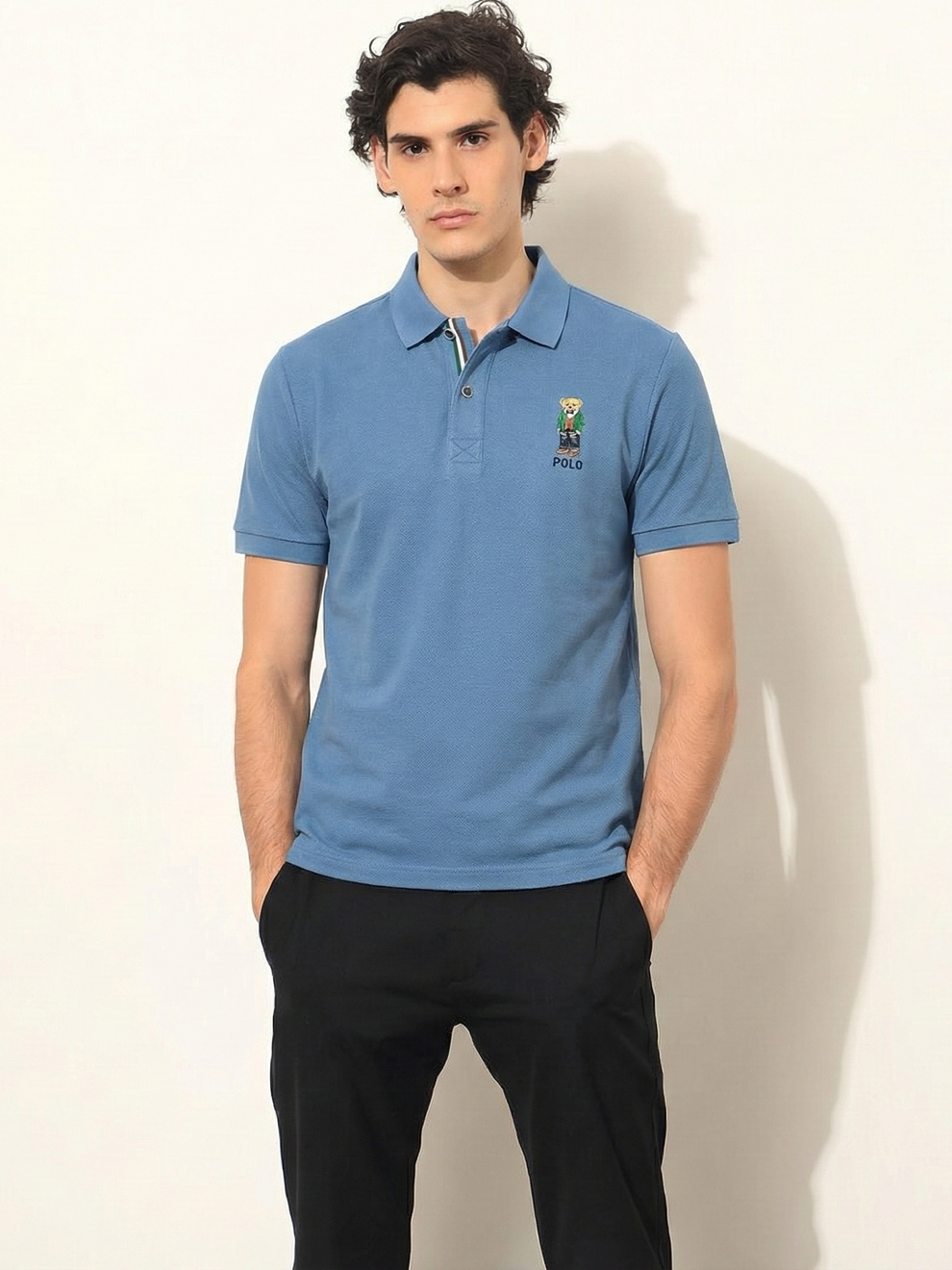 Man wearing a blue polo shirt with a logo on a plain background