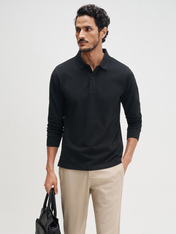 Man wearing a black long-sleeve polo shirt, beige pants, and black shoes on a white background