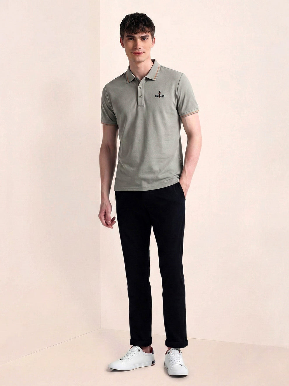 Man wearing a gray polo shirt and black pants on a beige background