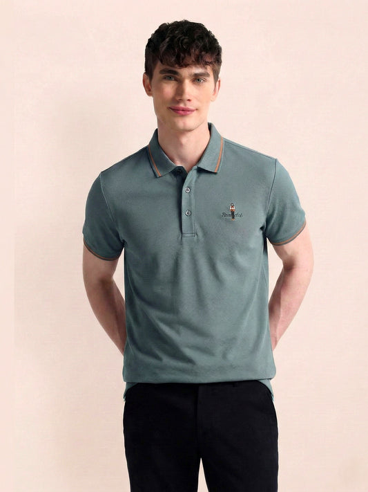 Man wearing a teal polo shirt with a small logo on a beige background