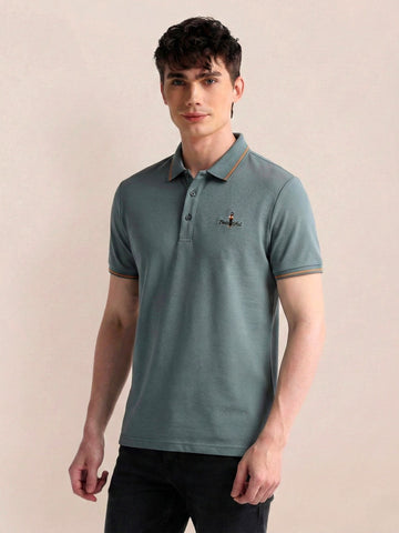 Man wearing a teal polo shirt with a small logo on a beige background