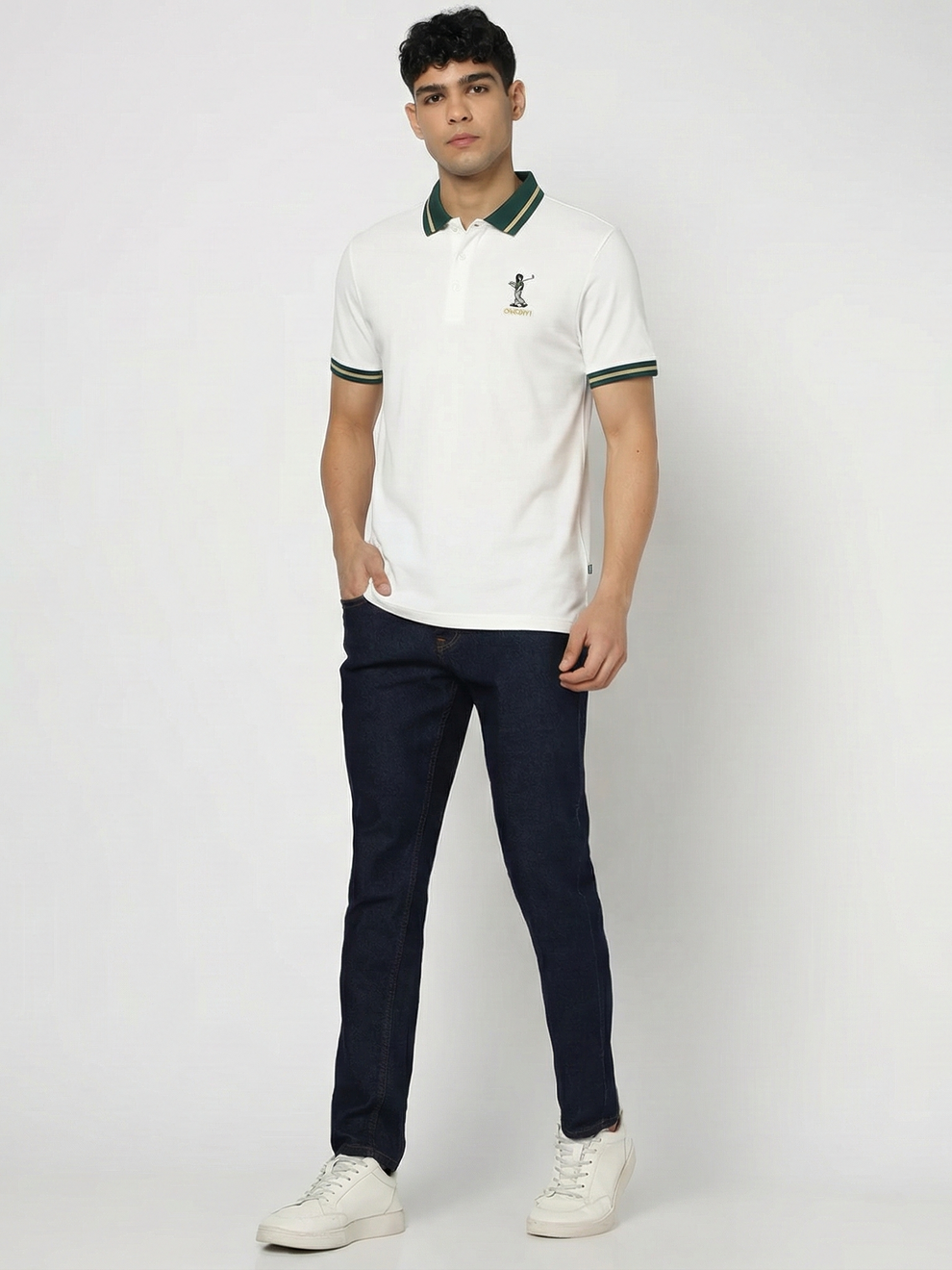 Man wearing a white polo shirt with green accents and dark jeans on a white background