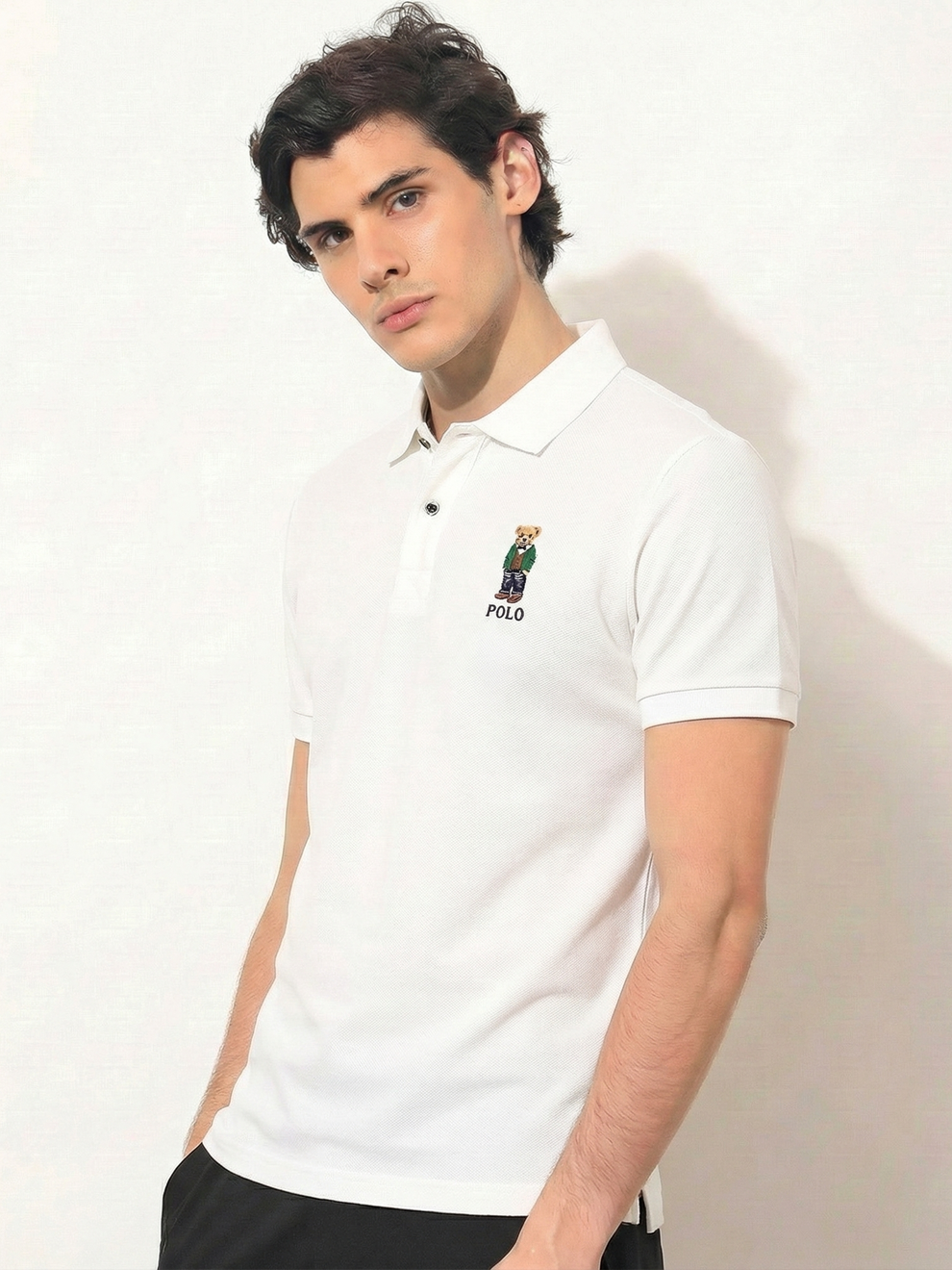 Man wearing a white polo shirt with a logo on a plain background